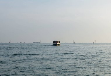 Venedik, İtalya - 07 Şubat 2026: Küçük balıkçı teknesi berrak bir gökyüzünün altında görünen uzak tekne ve şamandıralarla sakin sularda hareket ediyor