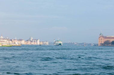 Venedik, İtalya - 07 Şubat 2026: Feribot Venedik sularından geçiyor, parlak bir gökyüzü altında kıyı şeridi boyunca tarihi mimari sergiliyor.