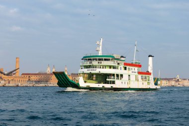 Venedik, İtalya - 07 Şubat 2026: Yeşil ve beyaz feribot tarihi binalar ve arka planda bulutlu bir gökyüzü ile denize açılıyor