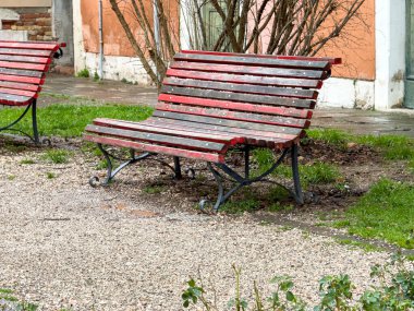 Çakıl yolundaki boş kırmızı halk parkı bankı.