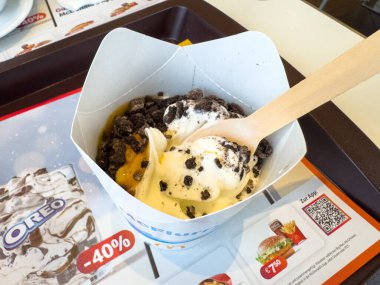 Villach, Avusturya - 29 Ocak 2026: Vanilyalı dondurma, ezilmiş kurabiye ve tanıtım grafikli fast food tepsisinde karamel sosuyla dolu tatlı bardağı