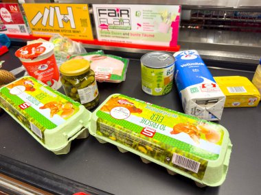 Villach, Avusturya - 29 Ocak 2026: Canlı ambalajlı bir süpermarket kasasında yumurta, konserve zeytin ve yoğurt gibi çeşitli sebze ürünleri