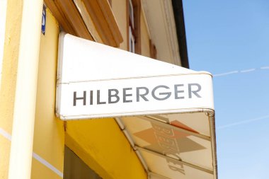 Villach, Avusturya - 06 Mart 2026: Hilberger, arka planda açık mavi gökyüzü olan sarı bir binanın ön cephesinde ticari kimliği vurguluyor.