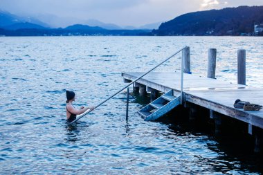 Dişi yüzücü, kışın tadını çıkarıyor. Alacakaranlıkta tahta iskelede yüzüyor..