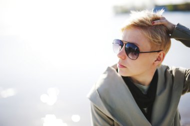 Suyun kenarında güneşlenirken genç güzel sarışın kız. Güneş gözlüğü takıyor. Dışarıda