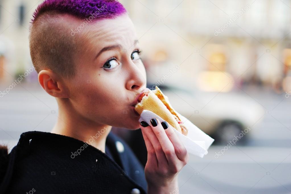 Charming Young Girl With Short Purple Hair Eats A Hot Dog On The