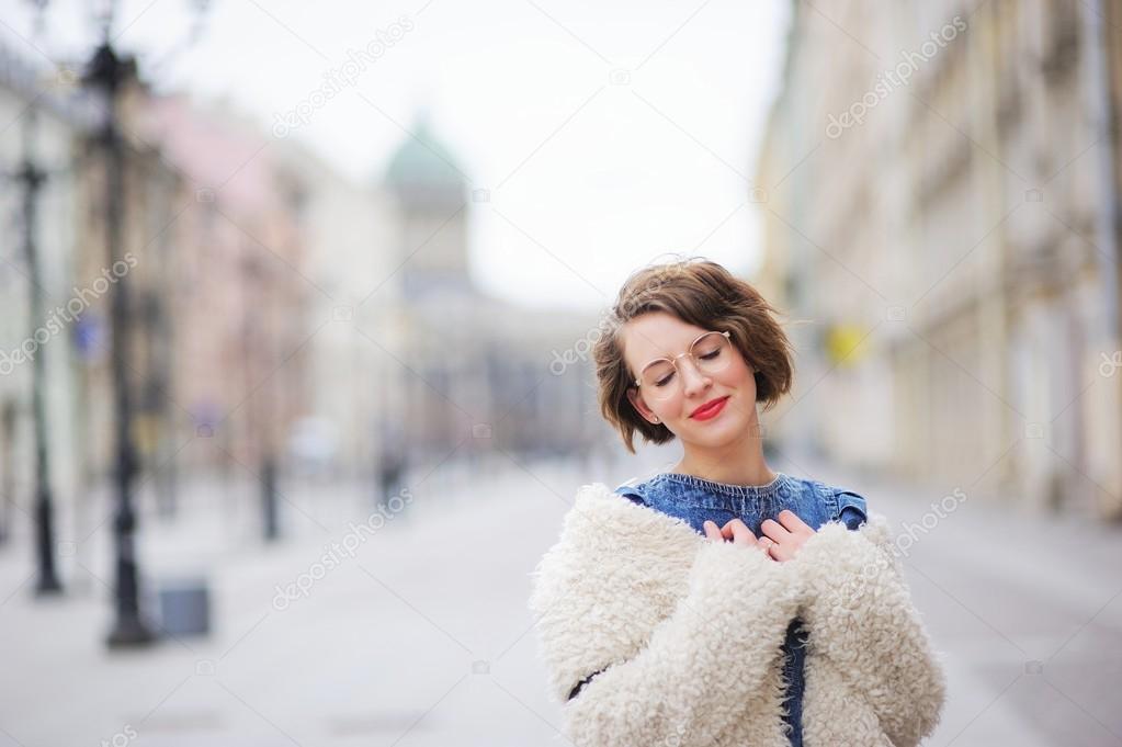 Beautiful young smiling girl posing on the boulevard in the center of St. Petersburg, closing her eyes in embarrassment.