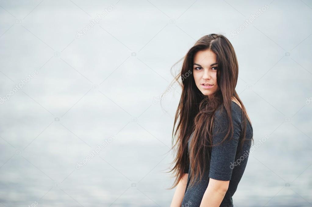 Portrait of beautiful brown-eyed girl with long, tangled from the wind, hair in a dark shirt on grey-blue background