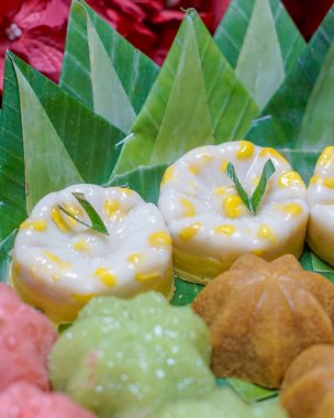 Endonezya geleneksel tatlılarının muz yaprakları üzerinde düzgünce sıralanmış yakın çekim makro fotoğrafı. Pirinç unu ve hindistan cevizinden yapılmış otantik Asya tatlı çeşitleri, mutfak tasarımı ve editoryal içerik için ideal..