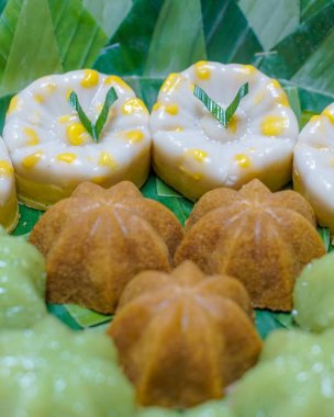 Endonezya geleneksel tatlılarının muz yaprakları üzerinde düzgünce sıralanmış yakın çekim makro fotoğrafı. Pirinç unu ve hindistan cevizinden yapılmış otantik Asya tatlı çeşitleri, mutfak tasarımı ve editoryal içerik için ideal..