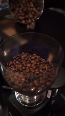 Roasted coffee beans pouring into a grinder hopper with warm lighting and soft bokeh. Great for F&B marketing, cafe branding, barista training, product packaging, and editorial use
