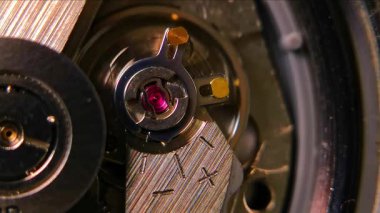 Otomatik bir saat kaçışının detaylı makro görüntüleri mücevher taşıyıcısını, denge çarkını, düzenleyiciyi ve metalik bileşenleri vurguluyor. Mühendislik, burs, imalat, zanaat ve zamanla ilgili görsel temalar için elverişli.