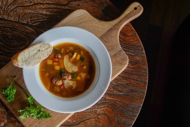 Köy tahtasında sunulan bir kase sıcak köfte ve sebze çorbası. Menüler, tarif blogları, mutfak reklamları, konforlu yemek konseptleri ve geleneksel ev yapımı yemek pişirme görselleri için idealdir.