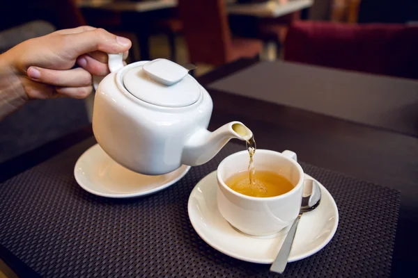 man pours tea from a white teapot in   Cup