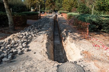Siper boyunca doğaçlama güvenlik çitleri olan yeşil ve yaya bölgesinde kazılmış uzun ve derin bir siperin yer aldığı inşaat mühendisliği projesi.