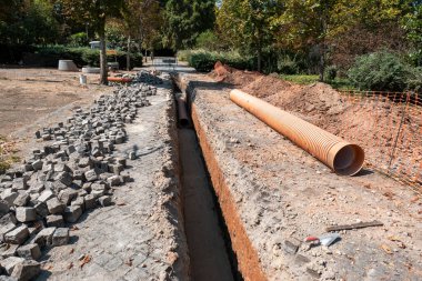Excavation of a deep trench in an urban area with piled-up cobblestones for the installation of new drainage or sanitation piping