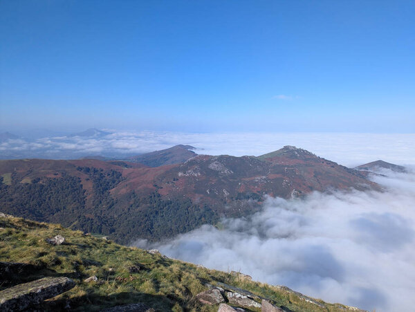 Stunning view of the autumnal mountains of Artzamendi in Itxassou, with a sea of fog under a blue sky in France