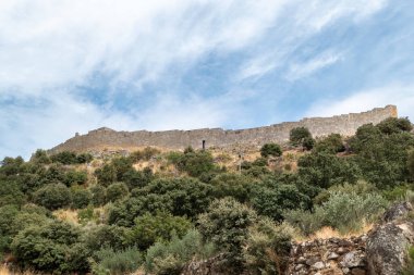 Portekiz 'de parçalı bulutlu bir gökyüzünün altında yoğun bitki örtüsüyle kaplı bir tepenin üzerine granit duvardan yapılmış ortaçağ Marialva Kalesi' nin heybetli duvarı dikildi.