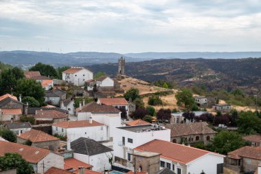 Penedono 'nun tarihi köyünün panoramik manzarası. Arka planda, Portekiz' in dağlık arazisi ve uzak rüzgar türbinleriyle çelişen bir tepenin üzerinde Ortaçağ Saat Kulesi bulunuyor.