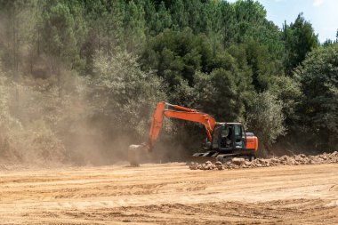 Otoyol inşaatında toprak hareketliliği üzerine çalışan kazıcı ağaçlık bir alanda yoğun bir toz bulutu oluşturuyor.