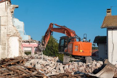 Eski bir binayı sökme operasyonu, enkaz ve kalıntı yığınları arasında ağır raylı makinenin altını çizmek.