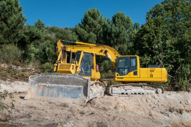 Bir orman bölgesinde bir tarımsal gölet inşaatında bir buldozer ve bir kepçeyle kazı ve toprak taşıma.
