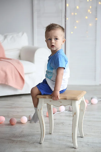 Bonito menino sentado em uma cadeira no quarto decorado — Fotografia de Stock