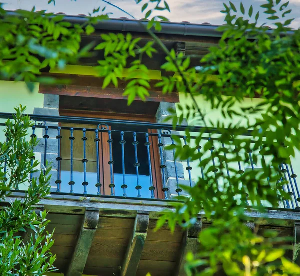 Yeşil defne bitkileriyle dekore edilmiş bir kulübe balkonu. Doğal ışık ve kırsal atmosferi olan sakin bir açık hava sahnesi.