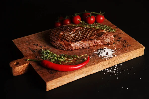 Kesme tahtasında ızgara et, tuz, biber, biberiye ve vişneli domates ve baharatlı ızgara et.