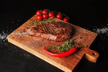 Kesme tahtasında ızgara et, tuz, biber, biberiye ve vişneli domates ve baharatlı ızgara et.