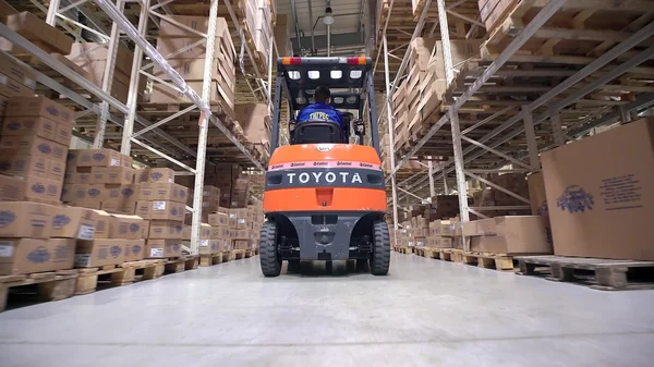 Las carretillas elevadoras se mueven entre grandes estantes metálicos en un almacén moderno y descargan paletas con cajas de cartón — Foto de Stock