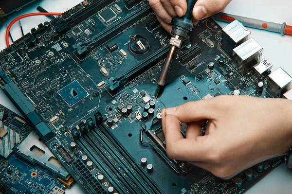 Un hombre sostiene una herramienta para reparar la electrónica, ensamblando manualmente una placa de circuito de soldadura. Fotos de stock