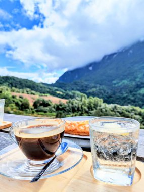Kapalı kahve fincanı ve ahşap masada serinletici bir bardak köpüklü su ve Chiang Mai, Tayland 'daki muhteşem yeşil Doi Luang Chiang Dao dağ manzarasının bulanık arkaplanı.