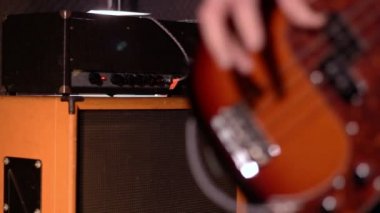 Bas gitarist. Bas çalmaya bir erkek eli yakın çekim için amplifikatör ve hoparlör kutusu olarak arka plan bulanıklık.