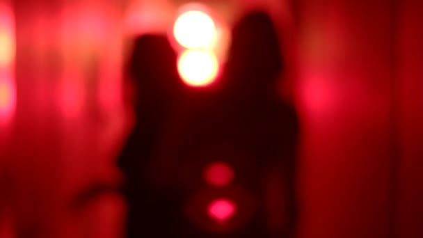 Silhouette of two sexy women dancing in a blurry, red corridor with her hands raised.