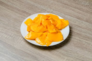 Ahşap bir masada taze mango dilimleri ile tabak.
