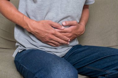 Kanepede oturan ve karnını acı içinde tutan bir adam. Midesi ağrıyan genç bir adam.