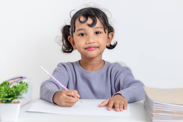 Умная маленькая азиатская девочка учится за своим столом.