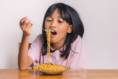 Evde bir tabak kızarmış eriştenin tadını çıkaran küçük bir kız.