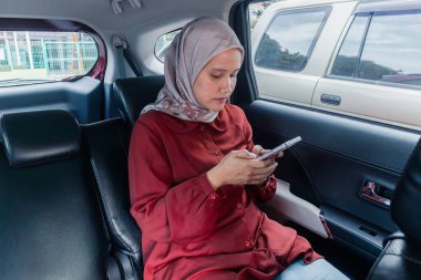 Genç bir Asyalı Müslüman kadın arabayla seyahat ederken akıllı telefonunu kullanıyor.