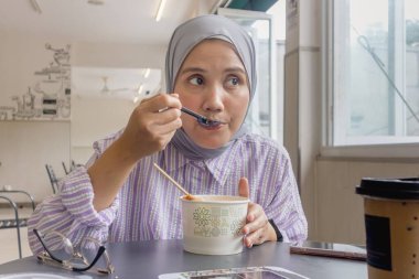 Genç bir Asyalı Müslüman kadın sipariş ettiği yemekleri tadıyor.
