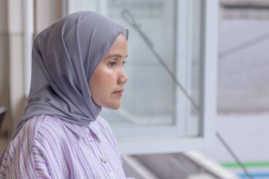 Genç bir Asyalı Müslüman kadın bir kahve dükkanının penceresinden dışarı bakıyor.