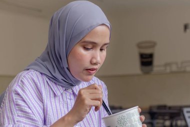 Genç bir Asyalı Müslüman kadın kaşıkla yemek yiyor.