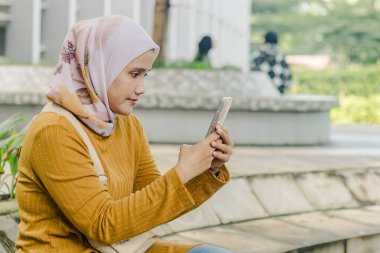 Endonezyalı genç bir müslüman kadın video görüşmesi yapıyor ya da dışarıda cep telefonuyla selfie çekiyor.
