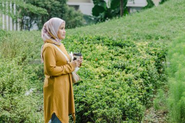 Parkta yürürken içki ve atıştırmalık taşıyan Endonezyalı genç bir Müslüman kadın.
