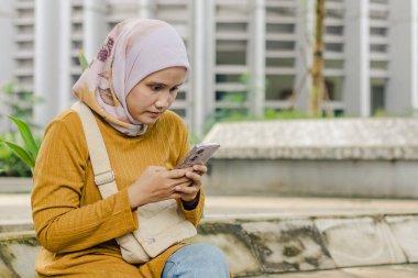Endonezyalı Müslüman bir kadın şehir parkında akıllı telefonuna mesaj yazıyor.