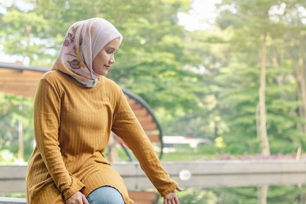 Endonezyalı genç bir Müslüman kadın şehir parkında balık havuzunun kenarında oturuyor.