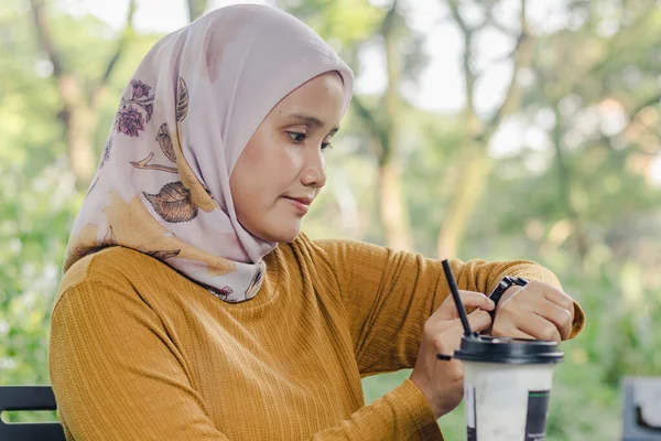 Endonezyalı Müslüman bir kadın parkta otururken saatine bakıyor.