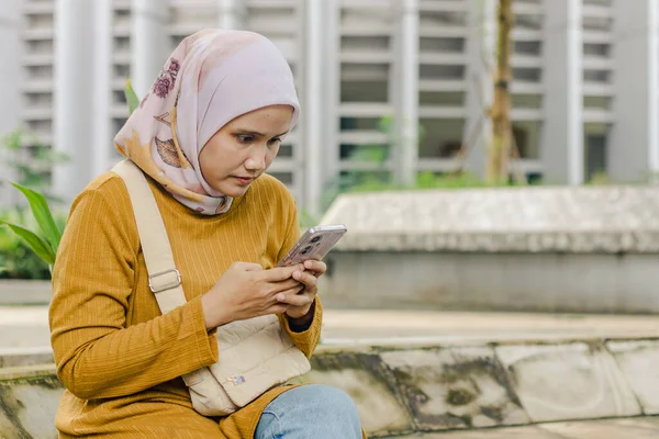 Endonezyalı Müslüman bir kadın şehir parkında akıllı telefonuna mesaj yazıyor.