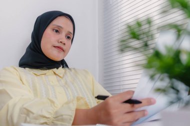 Genç bir Asyalı Müslüman iş kadını tamamlanmış çalışma dosyalarını inceliyor